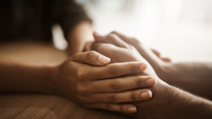 Images shows two people holding hands across a table