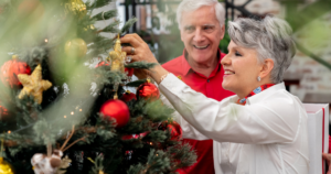 ‘How to approach Christmas When You’re New to Sight Loss’ article image of a couple decorating a Christmas tree. The man is smiling as the woman is placing a golden star ornament on the tree.