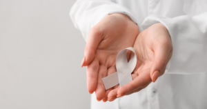 A white ribbon that symbolises Parkinson’s Awareness being held in the palms of a person wearing what looks like a white lab coat.